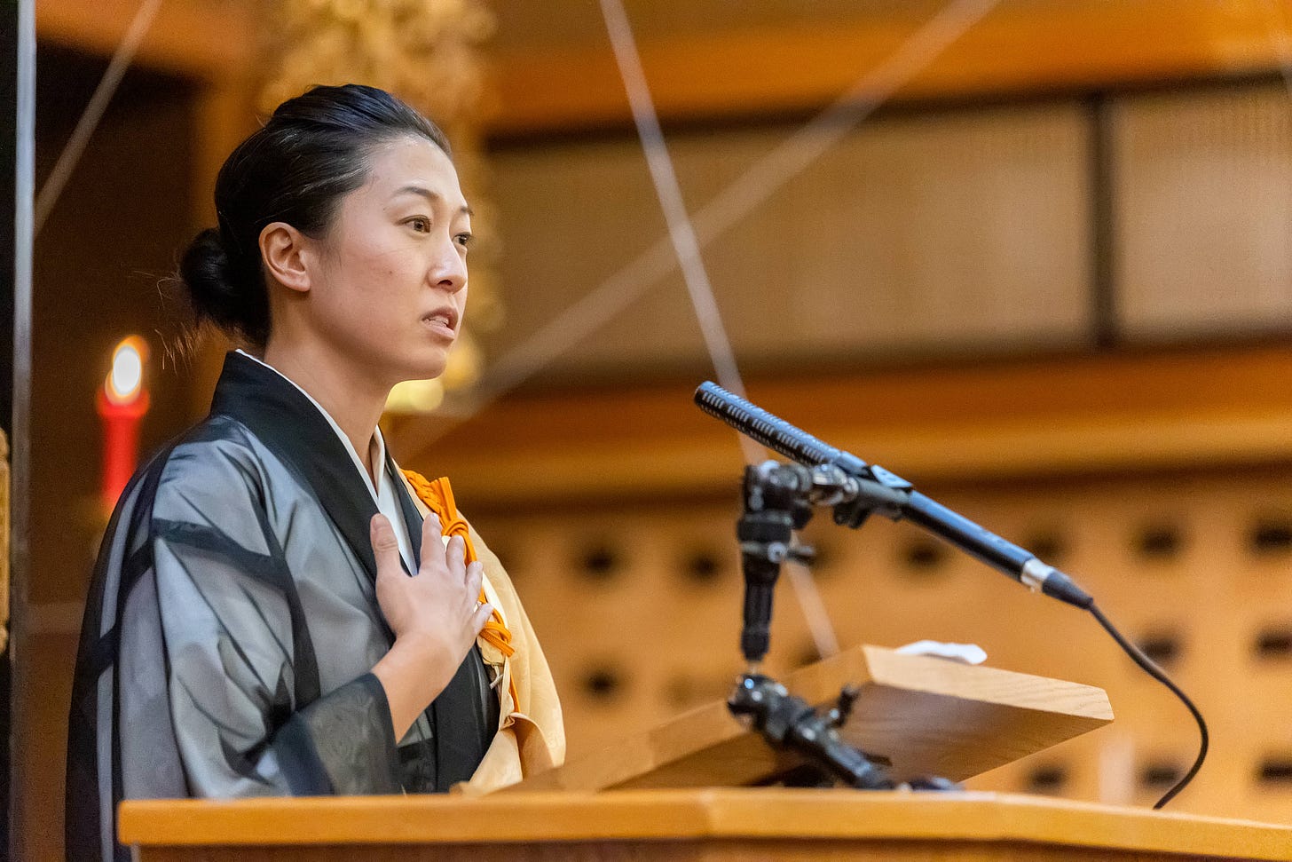 A Korean American woman speaking at a lectern, with her hand on her heart.