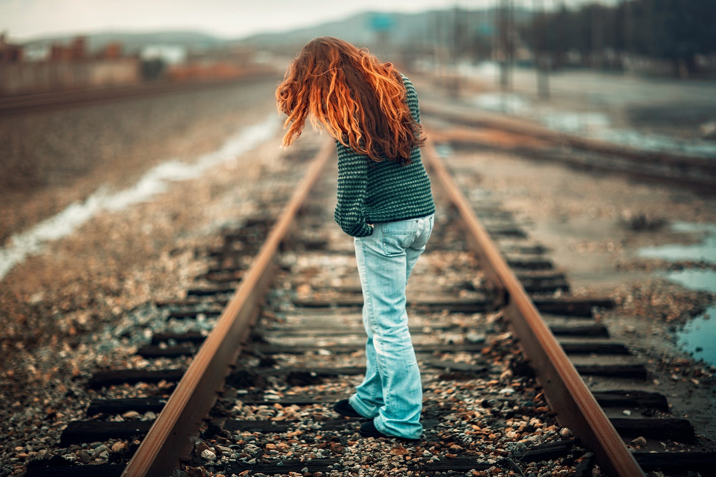 back view of girl with long red hair wearing denim jeans standing in middle of railroad track back view of girl with long red hair wearing denim jeans standing in middle of railroad track