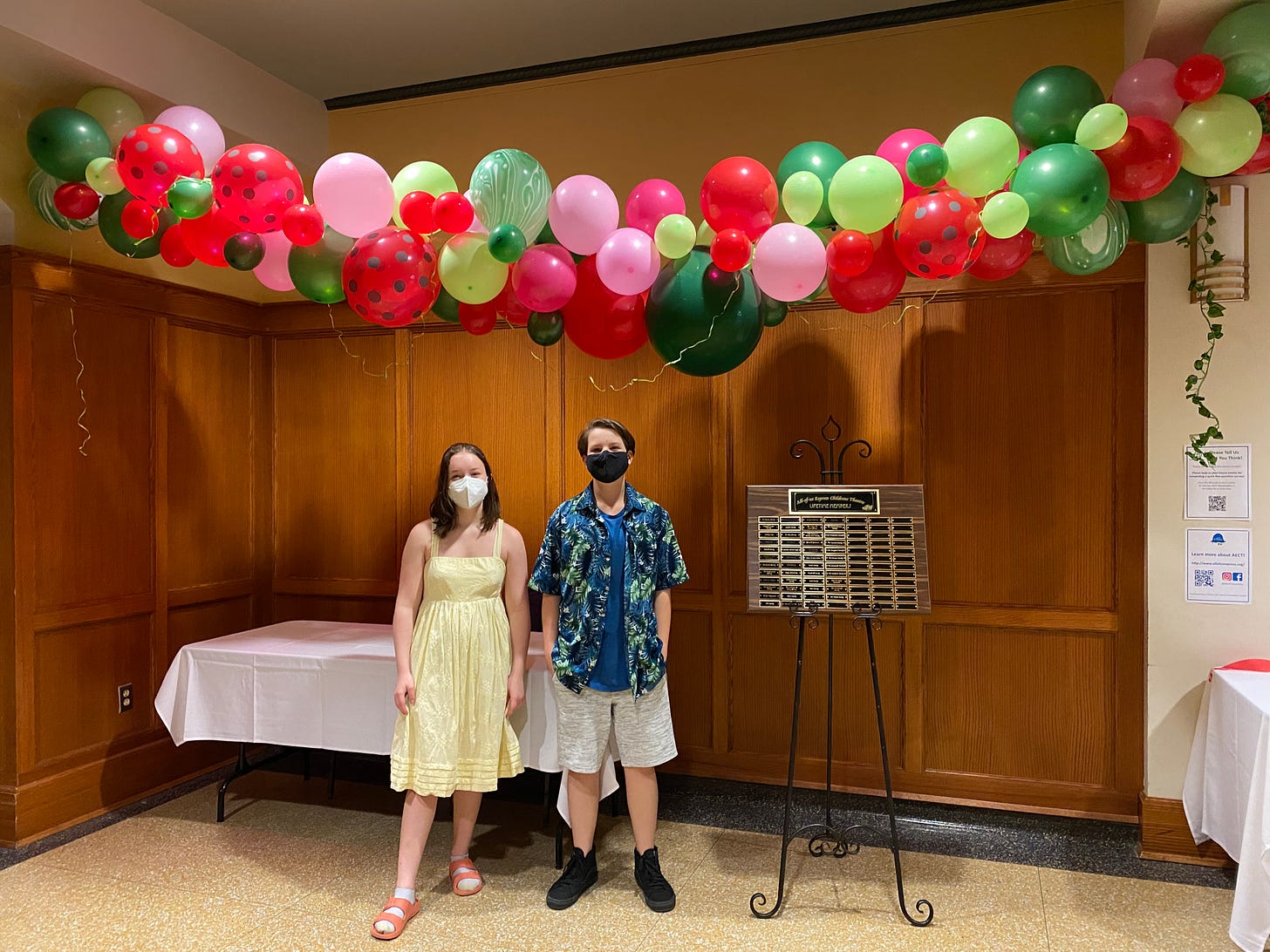 Two AECT members stand in front of a multi-colored balloon swag in the corner of the Hannah Theatre lobby