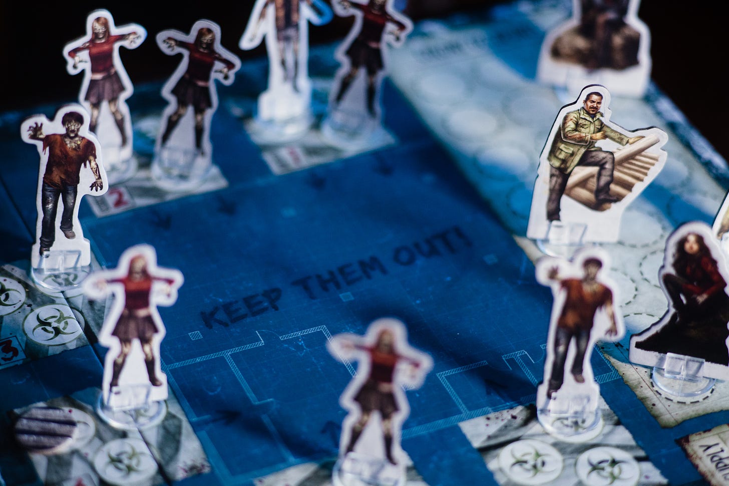 The board game Dead of Winter. Several zombie figures are surrounding a player base. Some character pieces are also pictured.