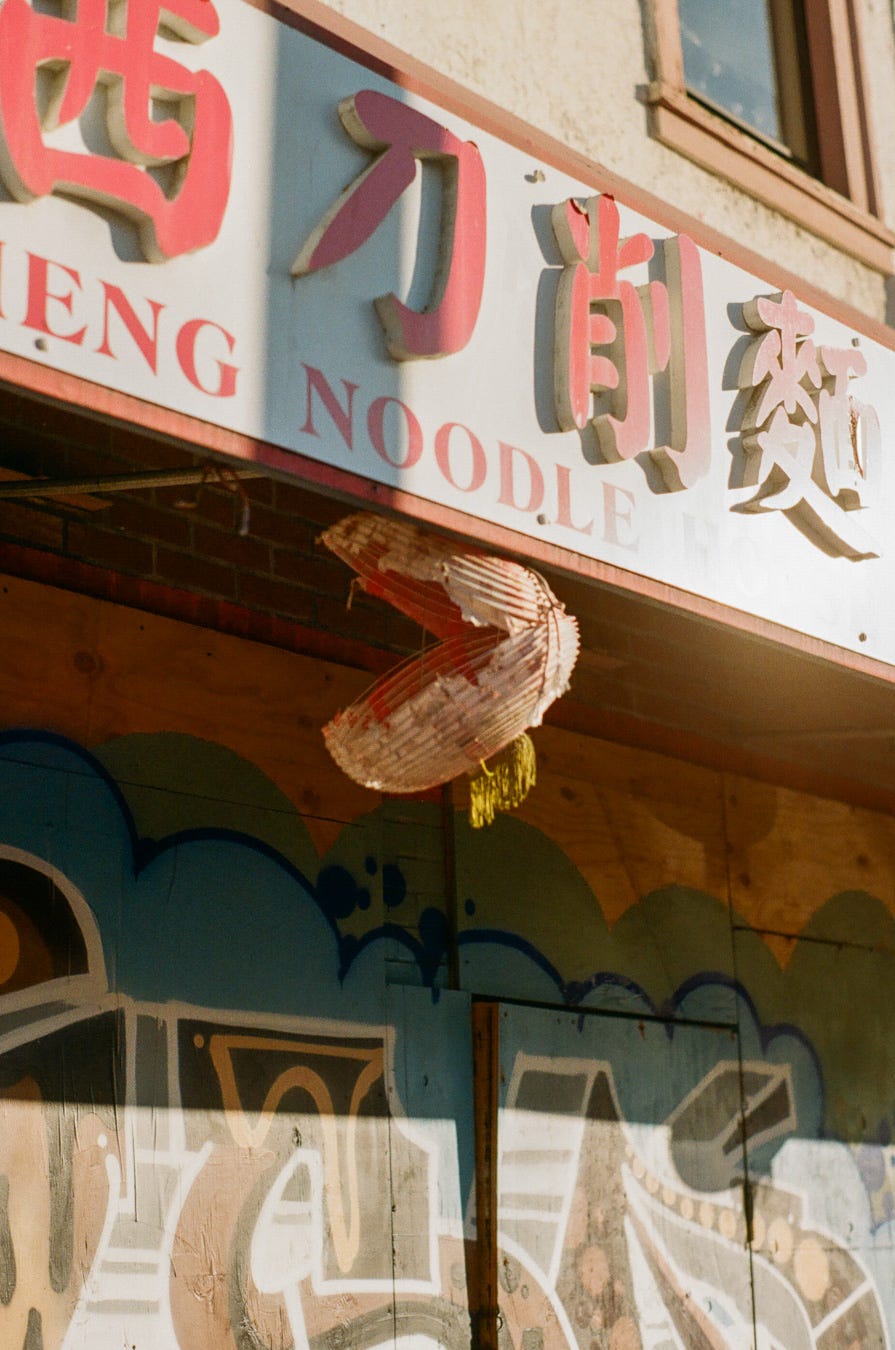 Photo of broken lantern hanging below restaurant sign with boarded up walls