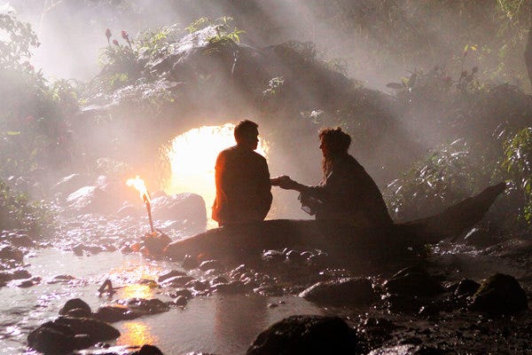 Jacob (Mark Pellegrino) sits outside a glowing cave. Mother (Allison Janey) hands him something to drink.