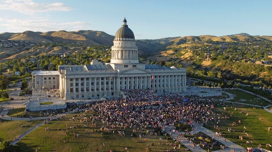 A large crowd of protesters gathers in front of a state capitol building.