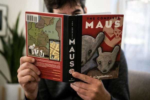 A man reads Maus, by Art Spiegelman, holding it in front of his face, which is obscured.