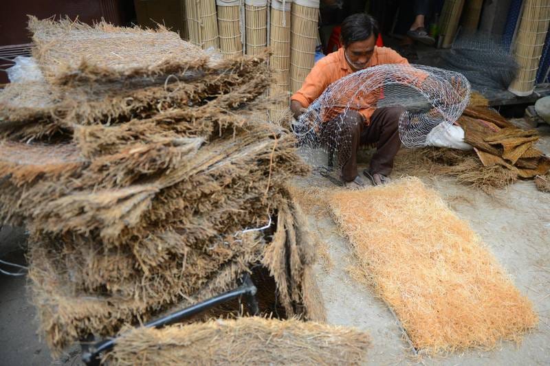 An Indian labourer prepares handmade air cooler pads at the roadside in Amritsar on May 9,2018. / AFP PHOTO / NARINDER NANU