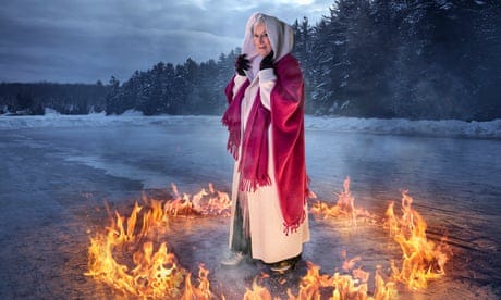 Margaret Atwood in a hooded coat and scarf, standing on an icy lake in the middle of a ring of fire