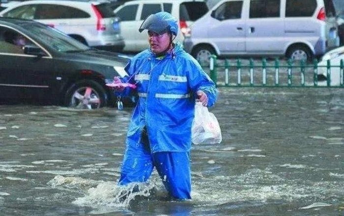 [Delivery rider wading through a flood from heavy rain]