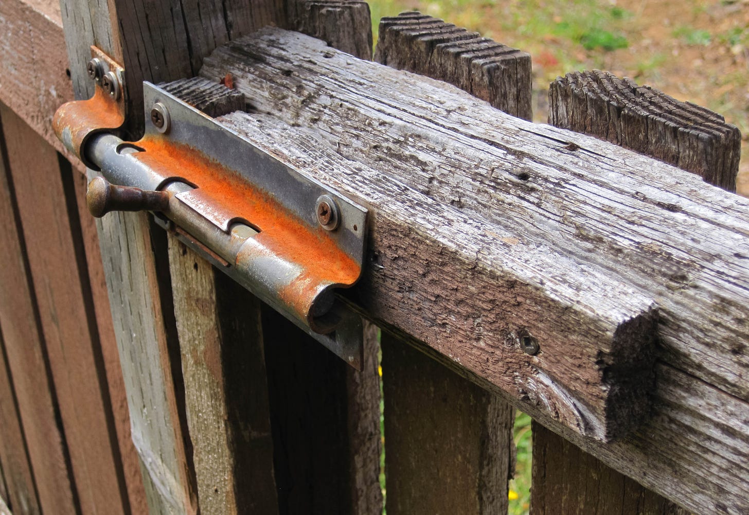 Aging, weather worn wooden fence with a rusty and oxidized slide lock on the gate