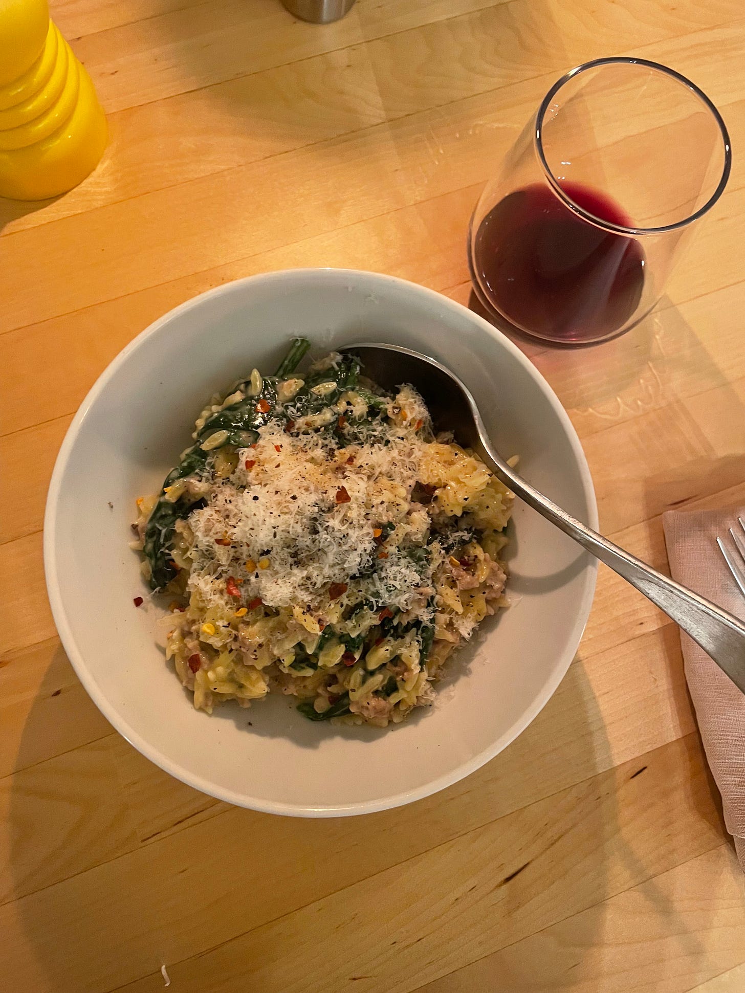 A bowl of creamy sausage orzo with spinach, freshly grated Parmesan cheese and plenty of chilli flakes. Enjoyed with red wine at the end of a sunny and busy spring day.