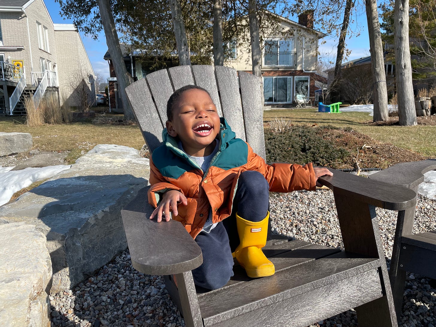 a Black boy in an orange coat opens his mouth, smiling, into the sun