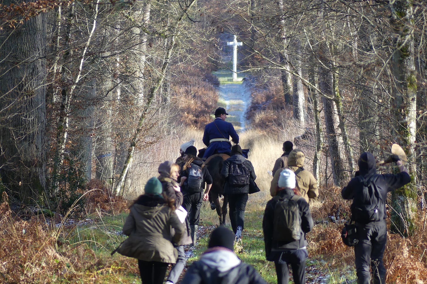 Hunt saboteurs chase a huntsman along a forest path, with a sign post in the background.