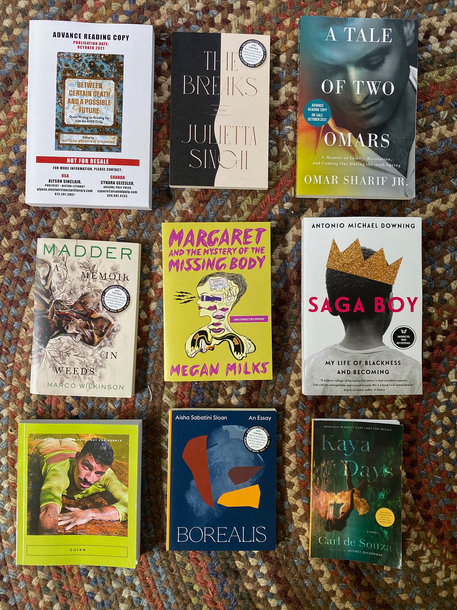 Nine books arranged in a rectangle on a braided rug: Between Certain Death and a Possible Future, The Breaks, A Tale of Two Omars, Madder, Margaret and the Mystery of the Missing Body, Saga Boy, Cuíer, Borealis, and Kaya Days.