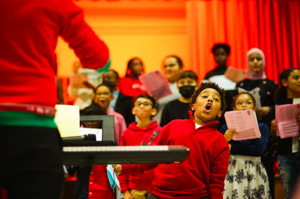 A photograph of a black and autistic 10 year old boy at his 4th grade winter concert singing gleefully.