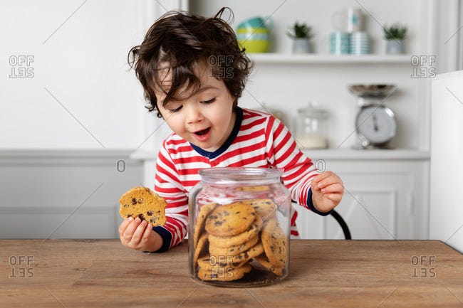 Happy young boy getting biscuits from cookie jar on kitchen table stock  photo - OFFSET
