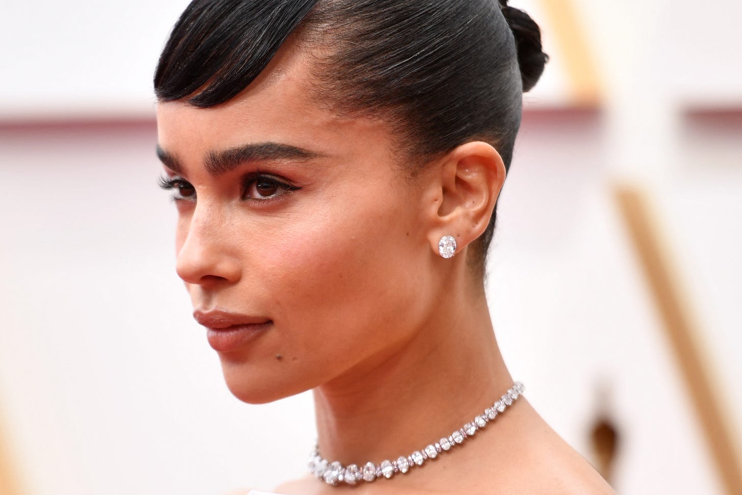 Zoe Kravitz with her hair in a bun and wearing diamond earrings and a necklace.