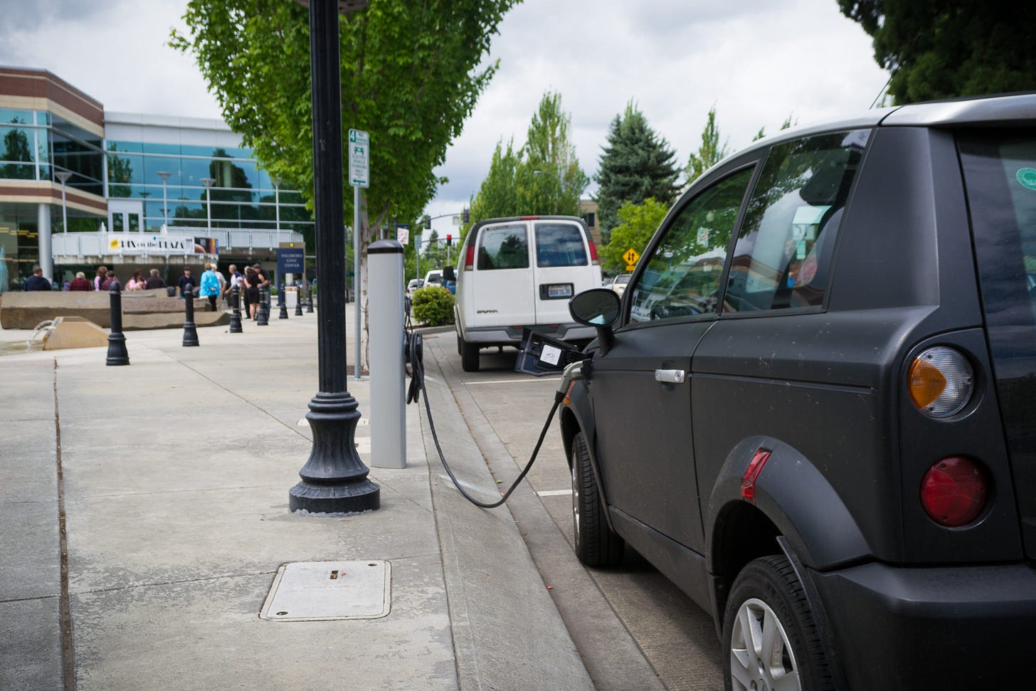 An electric vehicle, facing away from the camera, charging at a roadside electric vehicle charging point