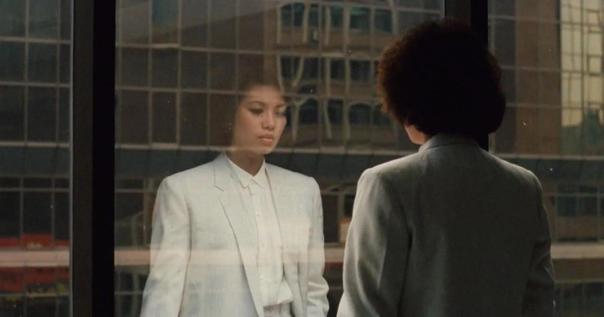 Movie still from Taipei Story. A woman business attire looks out a window, her reflection in the glass.