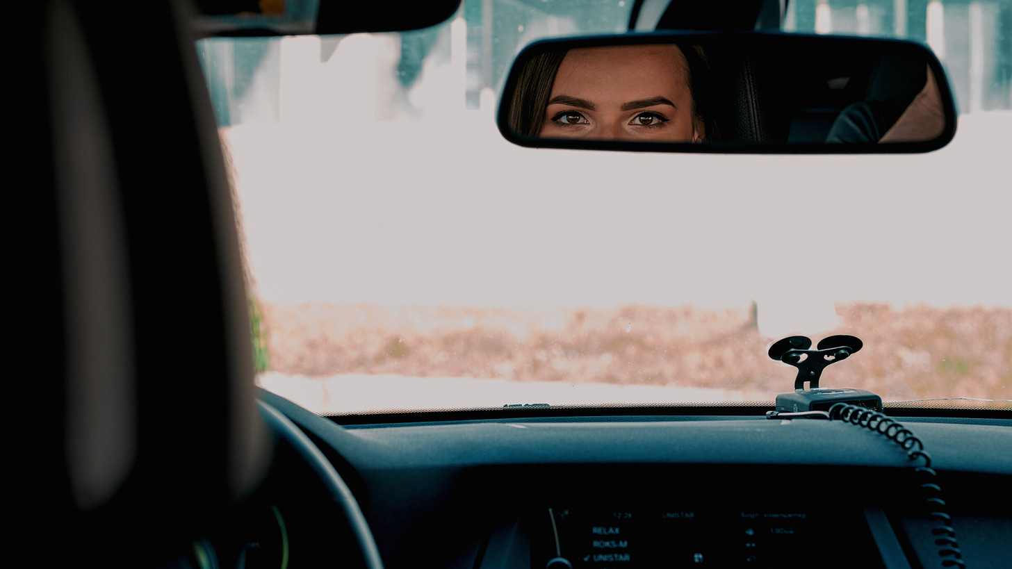 Dark haired, brown eyed woman eyes reflected in a rearview mirror