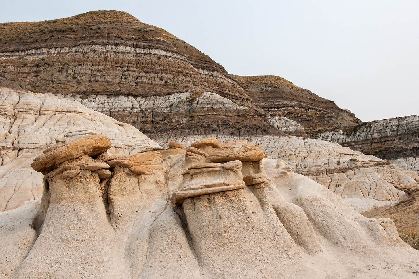 orange-topped hoodoos with crackling earth in front of a striped badlands hillside studded with scraggly brush