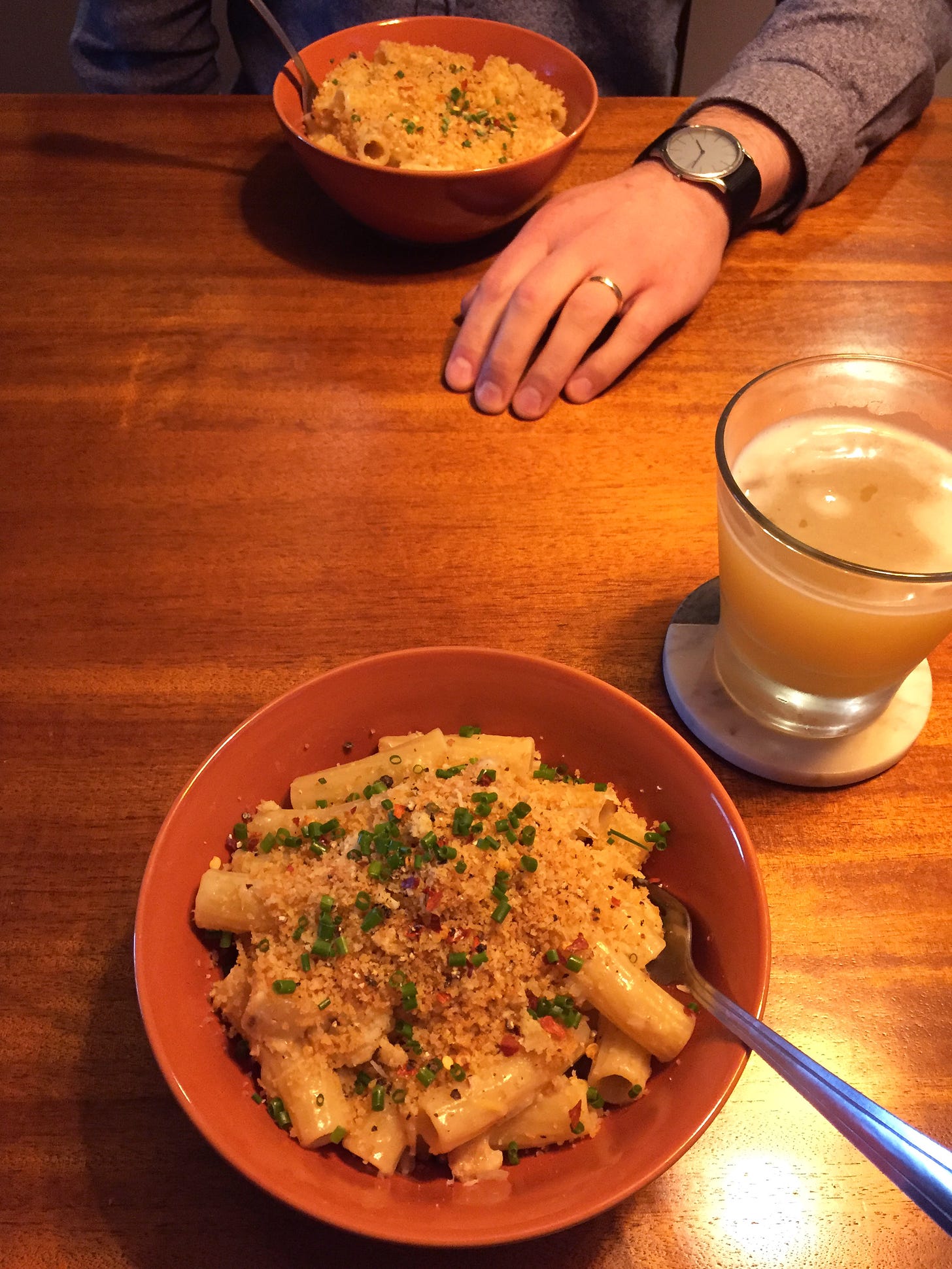 Two orange bowls across from each other on a table, each filled with creamy rigatoni and cauliflower, topped with breadcrumbs and chives. 