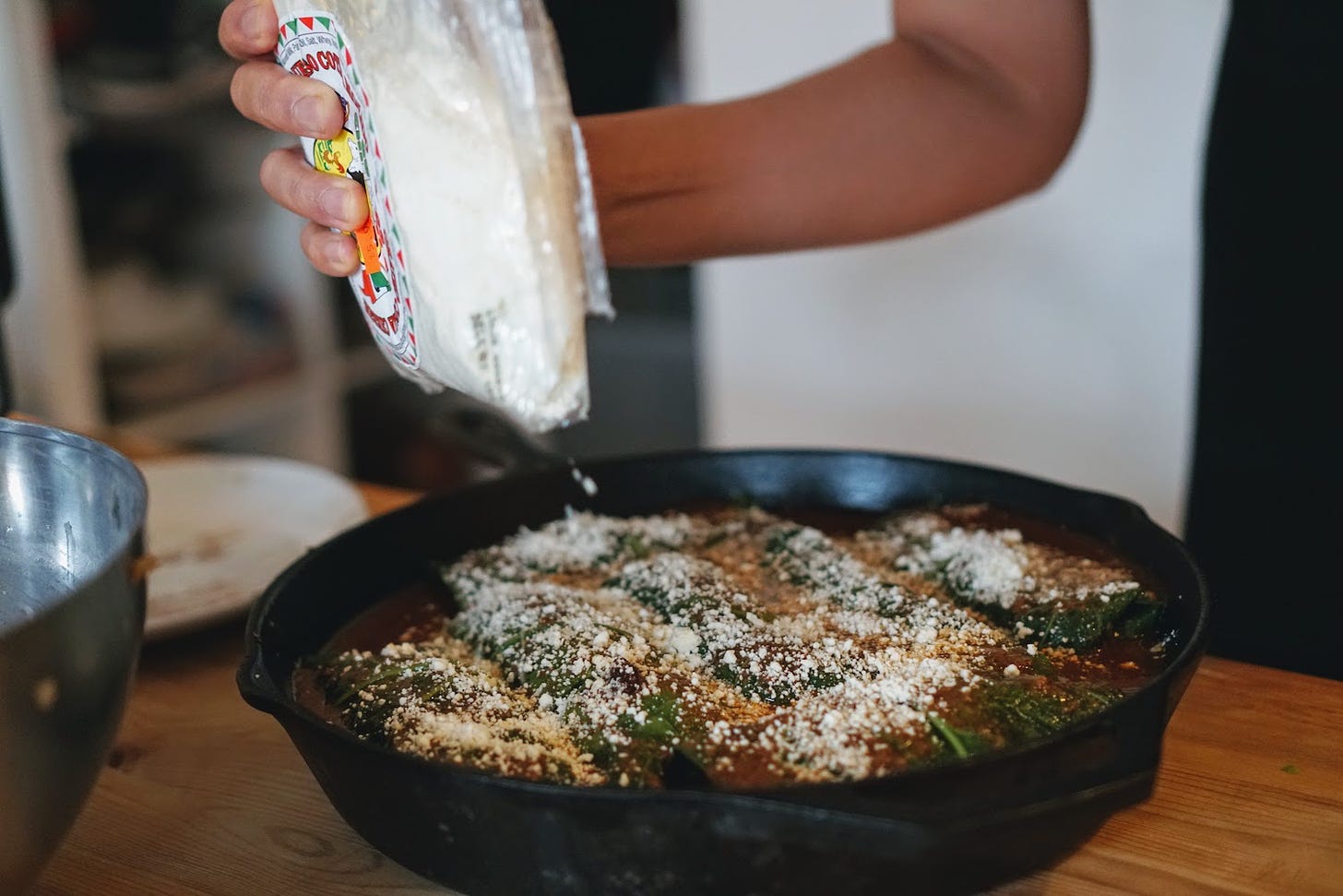 Sprinkling cotija cheese onto collared green enchiladas in a cast iron pan
