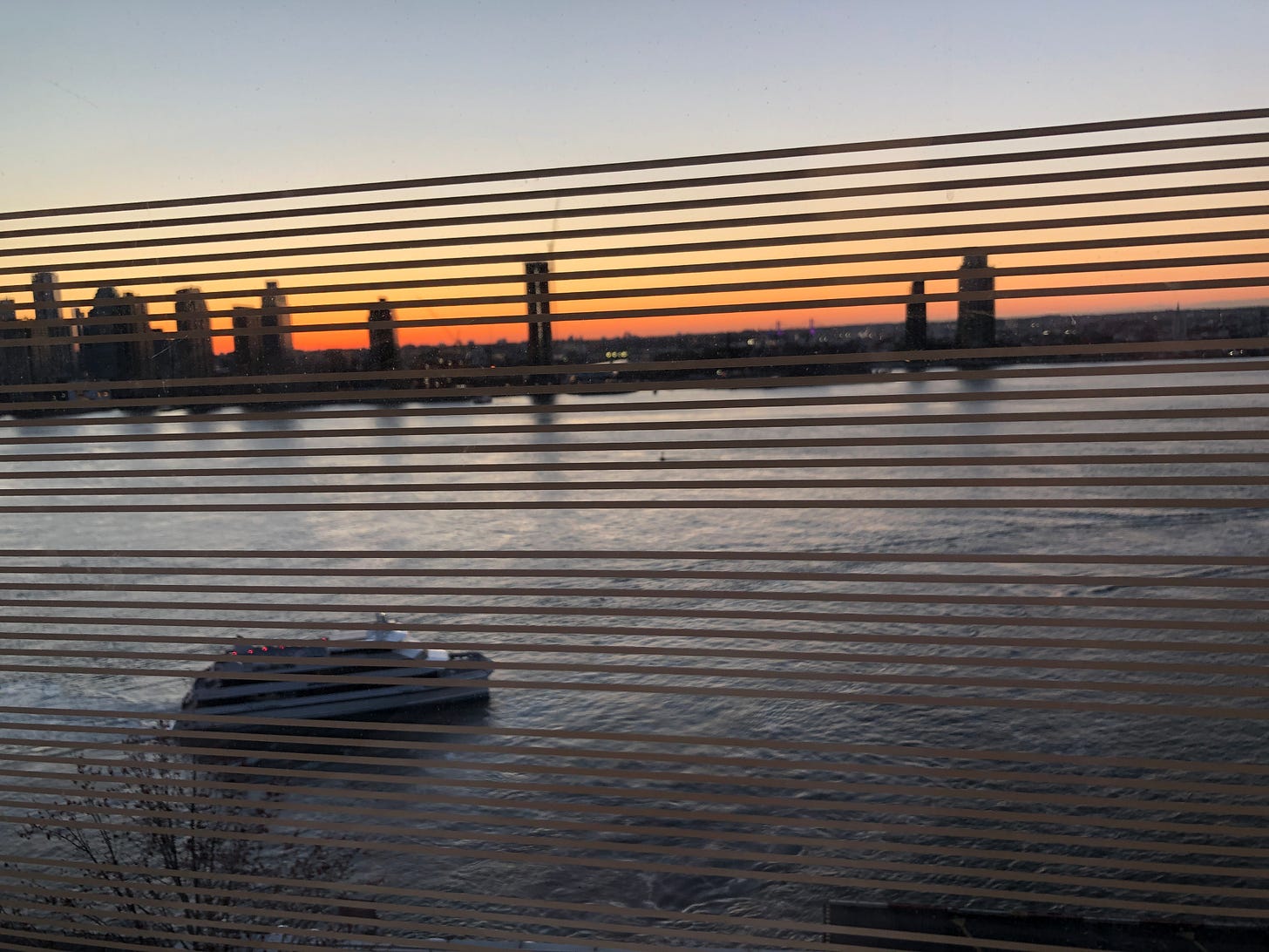 A view through window blinds of the sunrise over the East River.