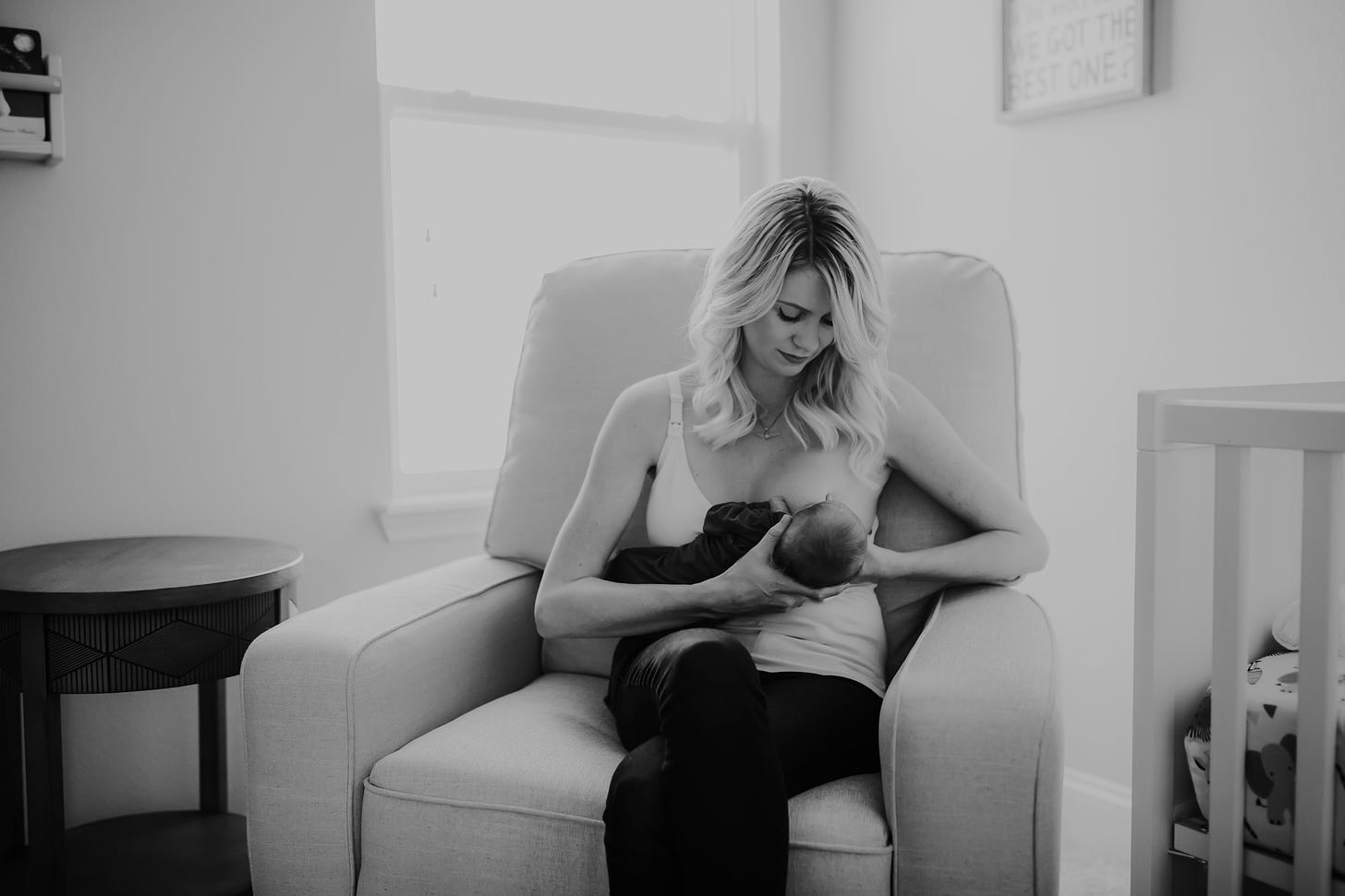 A black and white photo of Emily breastfeeding her newborn, Rowan in the baby's nursery.