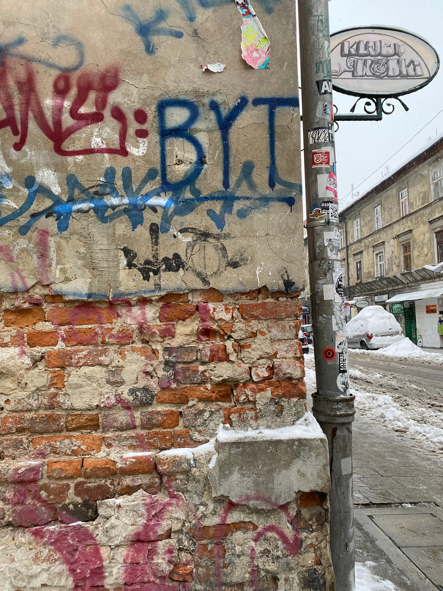 A graffitid urban wall. The pipe next to the wall is full of stickers. In the background, there is snow and ice everywhere.