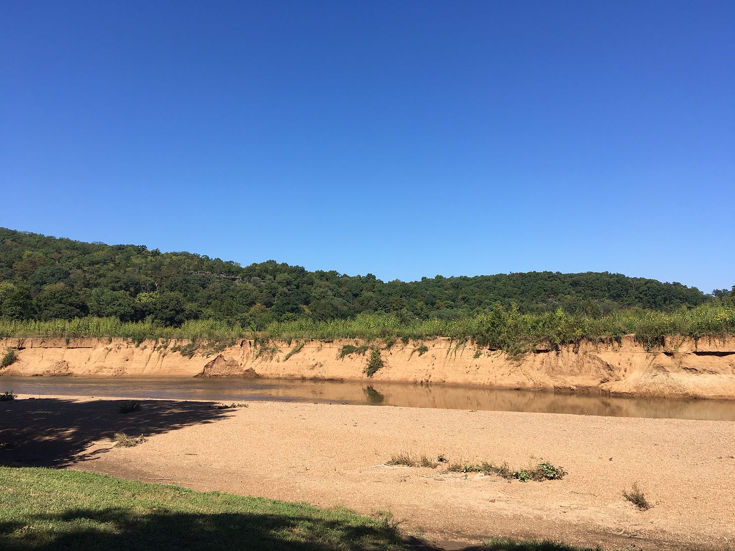 A river with a beach on one side and a bank of light tan soil on the other under a blue sky