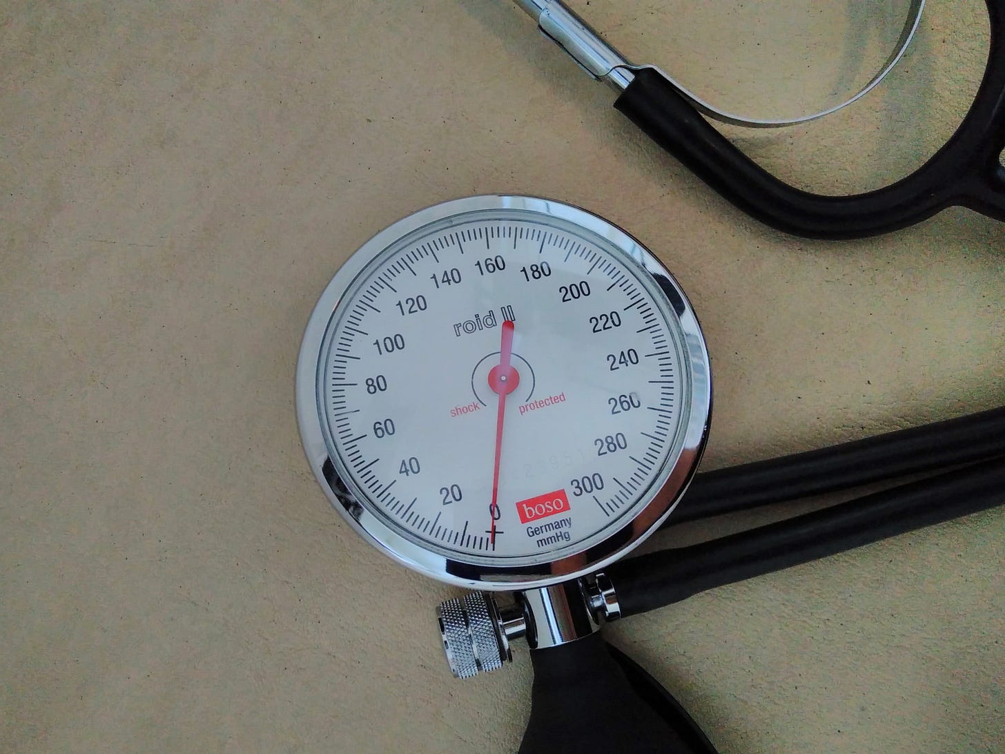 Das Bild zeigt Ausschnitte eines Blutdruckmessgeräts, dessen Zeiger null zeigt, und eines Stethoskops. 