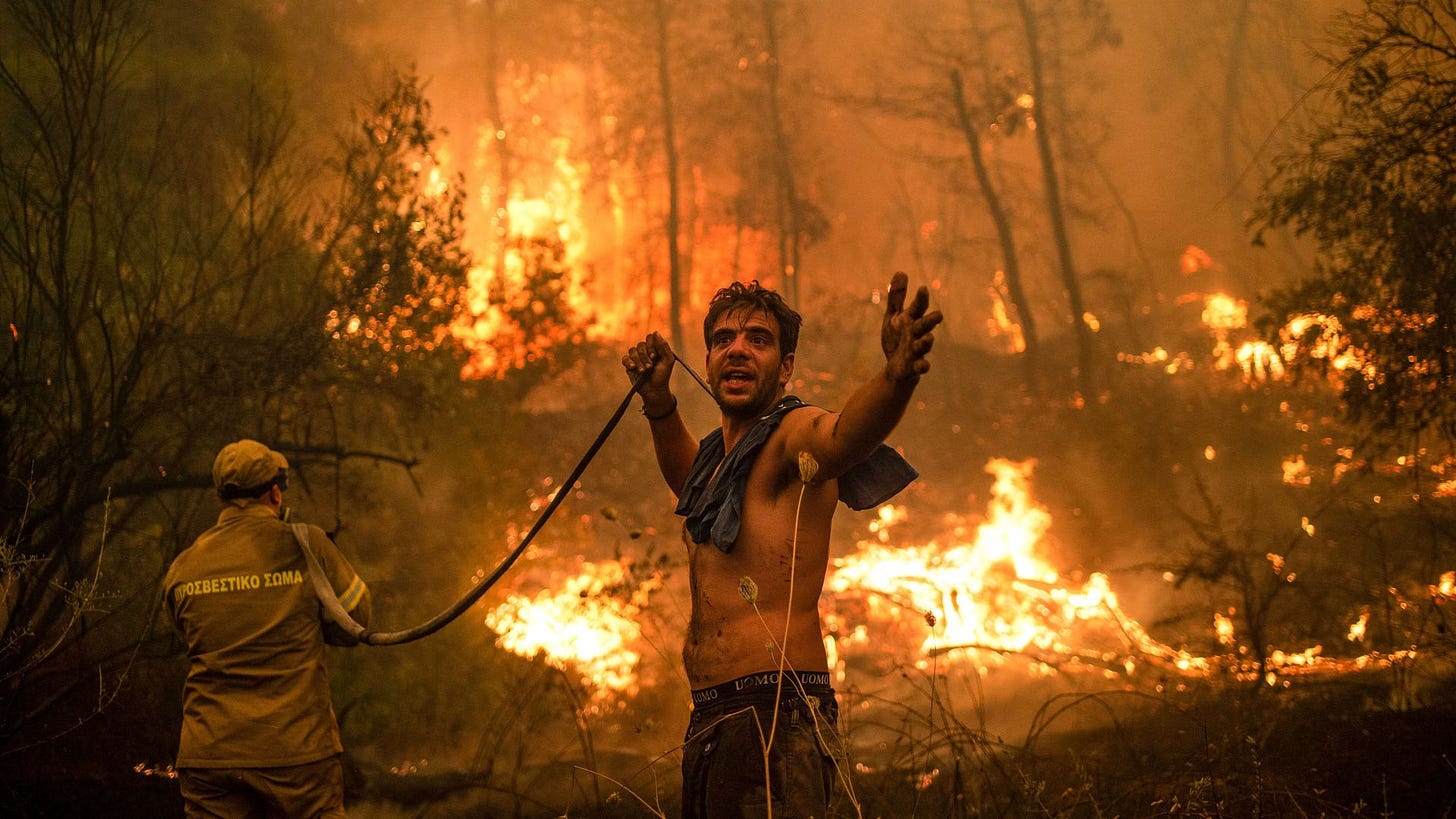 2021 年 8 月 8 日，一名当地居民在试图扑灭靠近希腊第二大岛埃维亚（Euboea）岛上的森林火灾时，举着一根空水管做手势（来源：Angelos Tzortzinis / AFP via Getty Images）