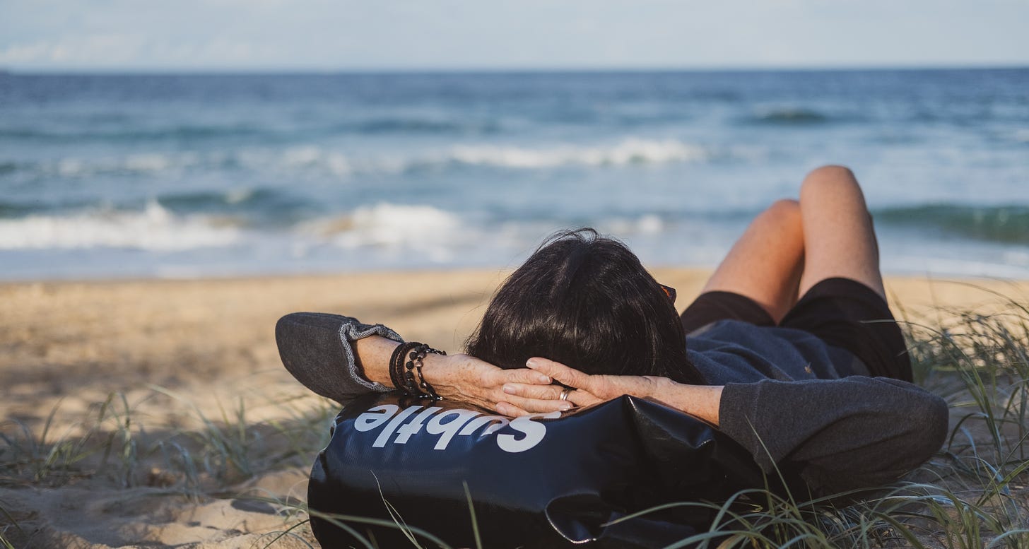 A person rests their head on a bag as they lay on the beach watching the waves