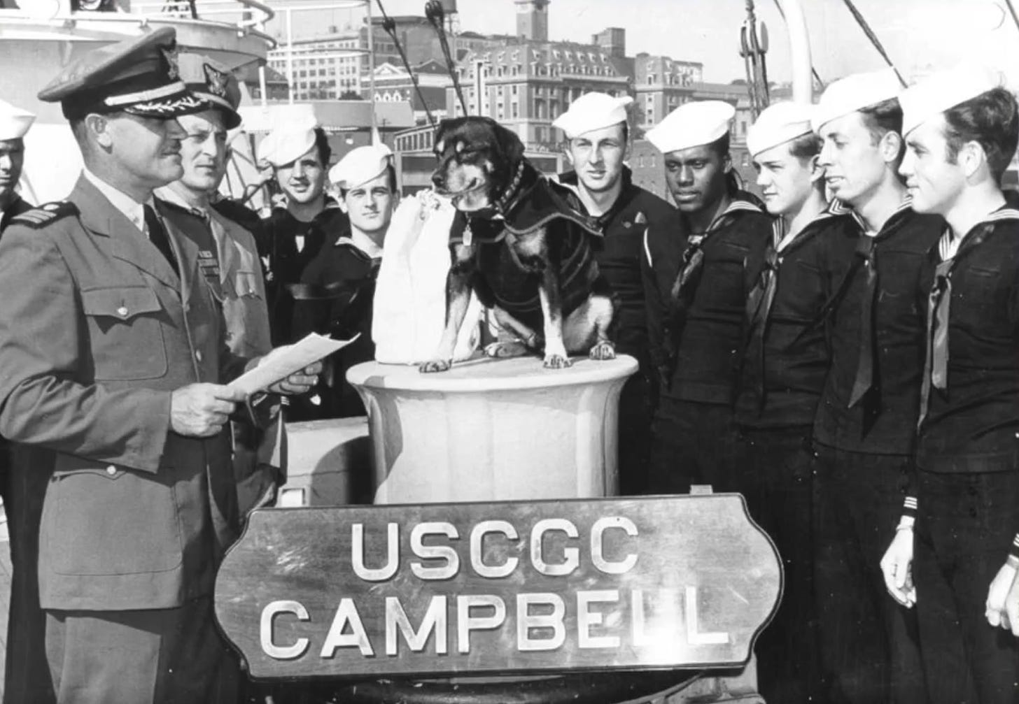 Sinbad sits on a pedestal surrounded by his crewmates.  A "USCGC Campbell" sign appears in the foreground.