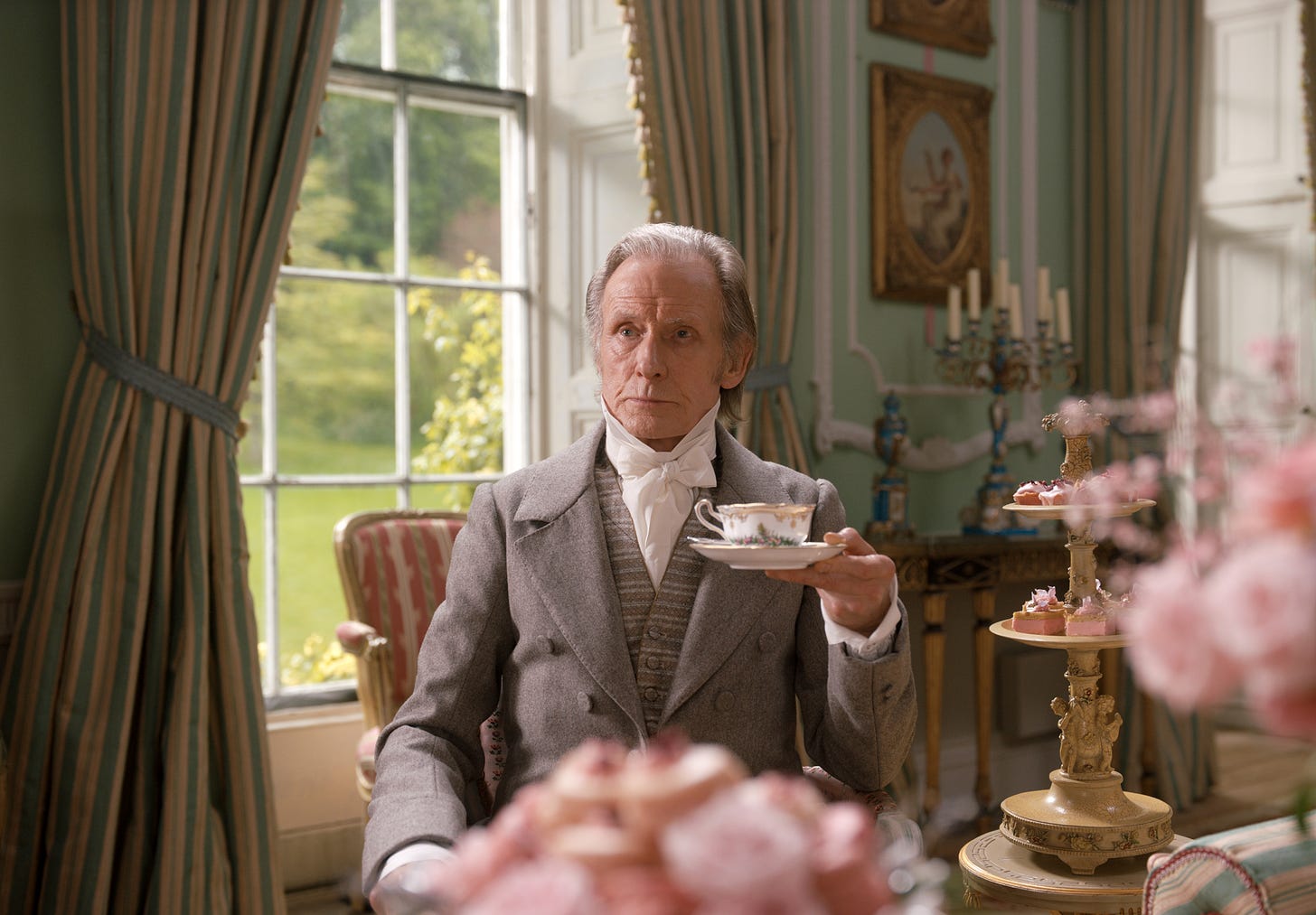 Bill Nighy as Mr. Woodhouse sits upright in a drawing room, holding a cup of tea and maintaining a look of consternation. The photo is from the 2020 Autumn de Wilde adaptation of Jane Austen's 'Emma'. 