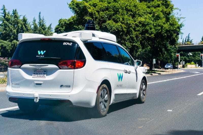 A Waymo-branded minivan prowls suburban streets.