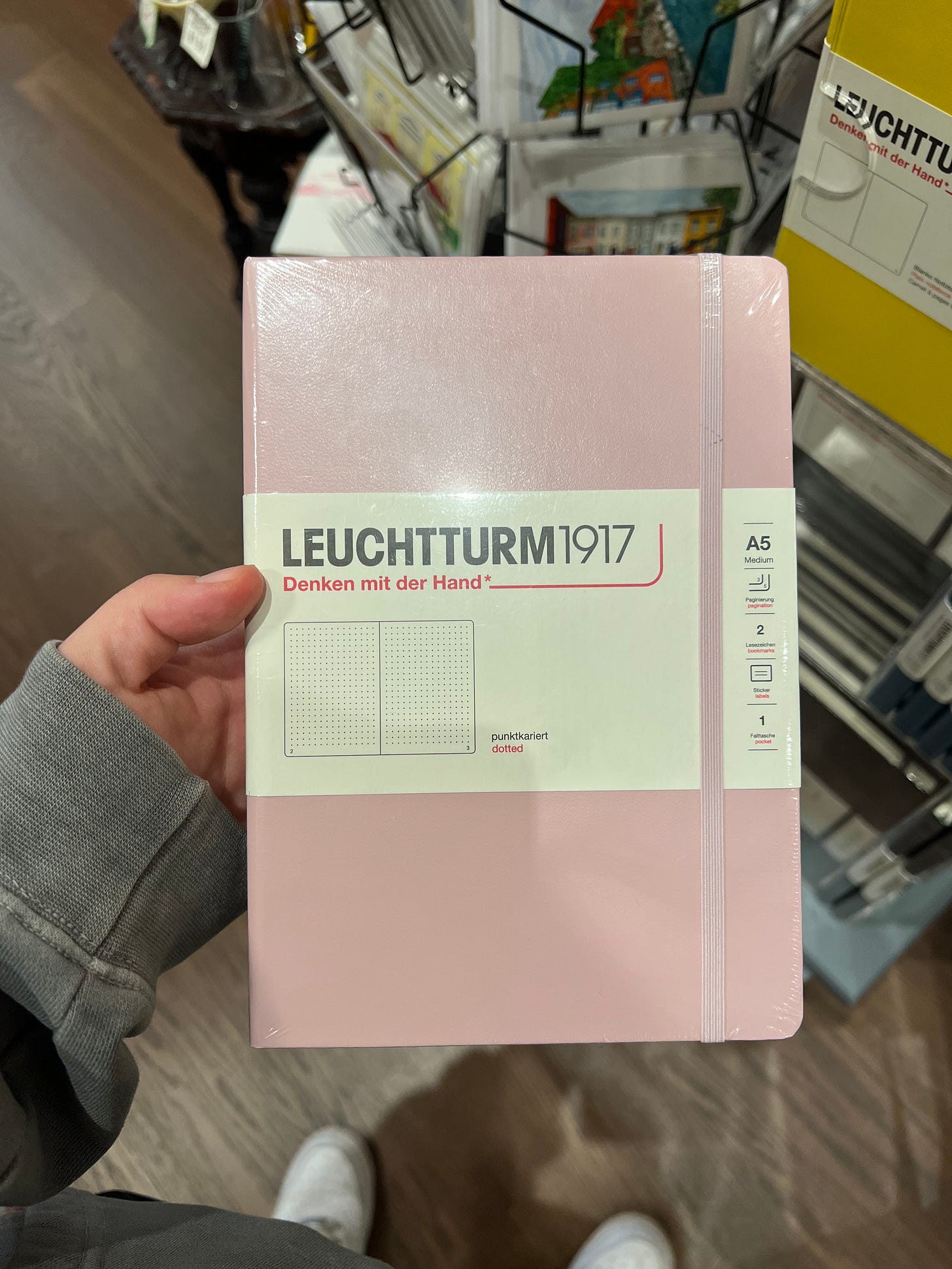 Noah's hand, white, holds a pale pink Leuchtturm1917 notebook. The background makes it clear that he is in a bookstore. 