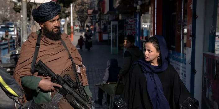 A Taliban fighter stands guard as a woman walks by him in Kabul