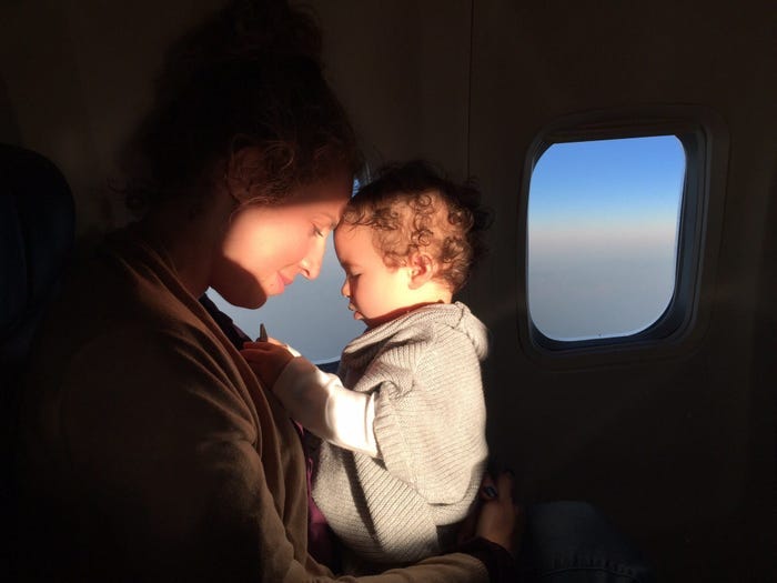 A woman and her baby on an airplane next to the window.