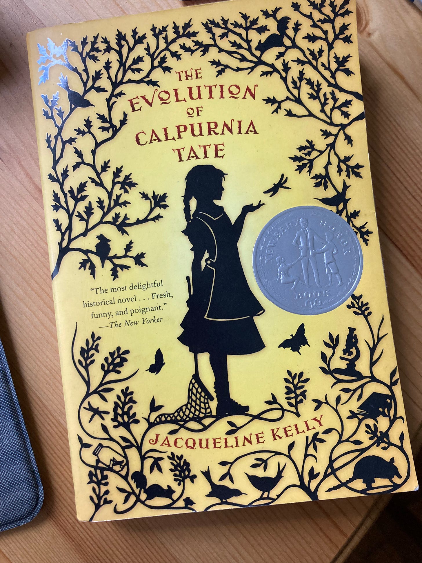 The Evolution of Calpurnia Tate bye Jacqueline Kelly book cover. A yellow book with black vines/leaves, animals and a girl. 