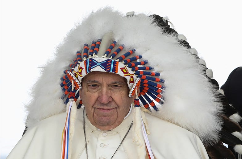 An elderly white man dressed in a white coat wears a headdress that is topped with long white and black feathers, decorated around his brow with blue, red, white, and yellow beading and a tassel draped down on either side of his face that is also in blue, red, white, and yellow. The elderly white man is looking out below him, and there is a white background behind him.