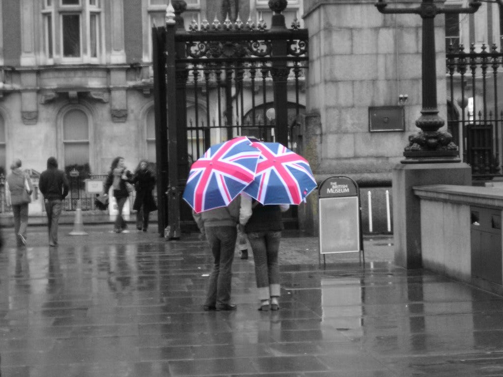 "Rule Britannia" by malias is licensed under CC BY 2.0. two people under umbrellas with the print of the British flag
