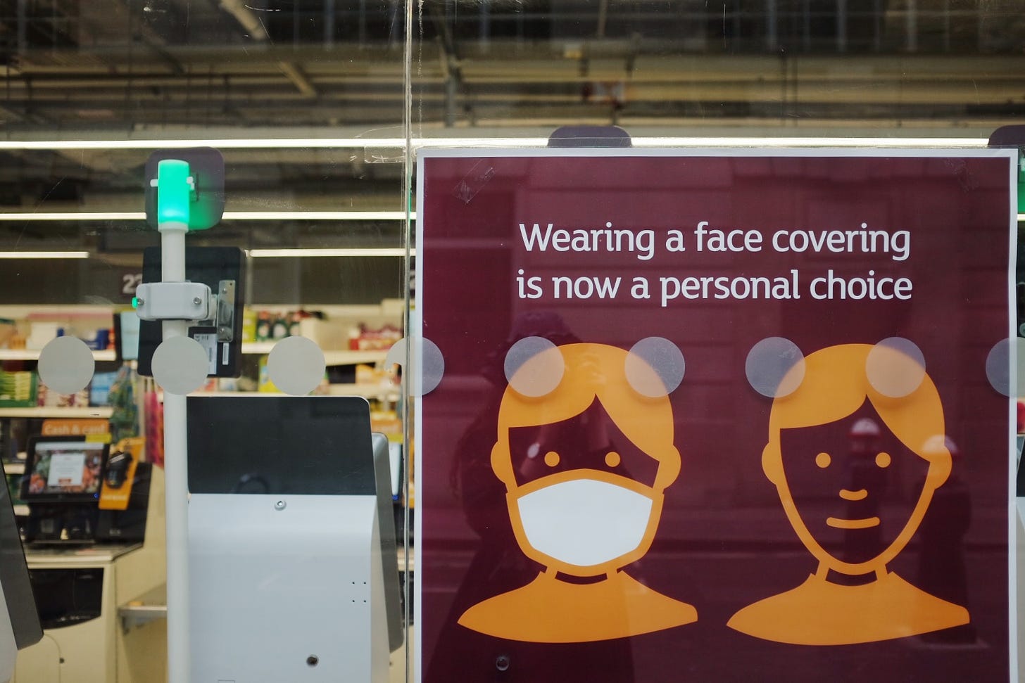 A large poster is displayed to the street from inside a supermarket in central London. The poster reads, "wearing a face covering is now a personal choice" and below the words are two simply-drawn faces, one wearing a mask and one not wearing a mask