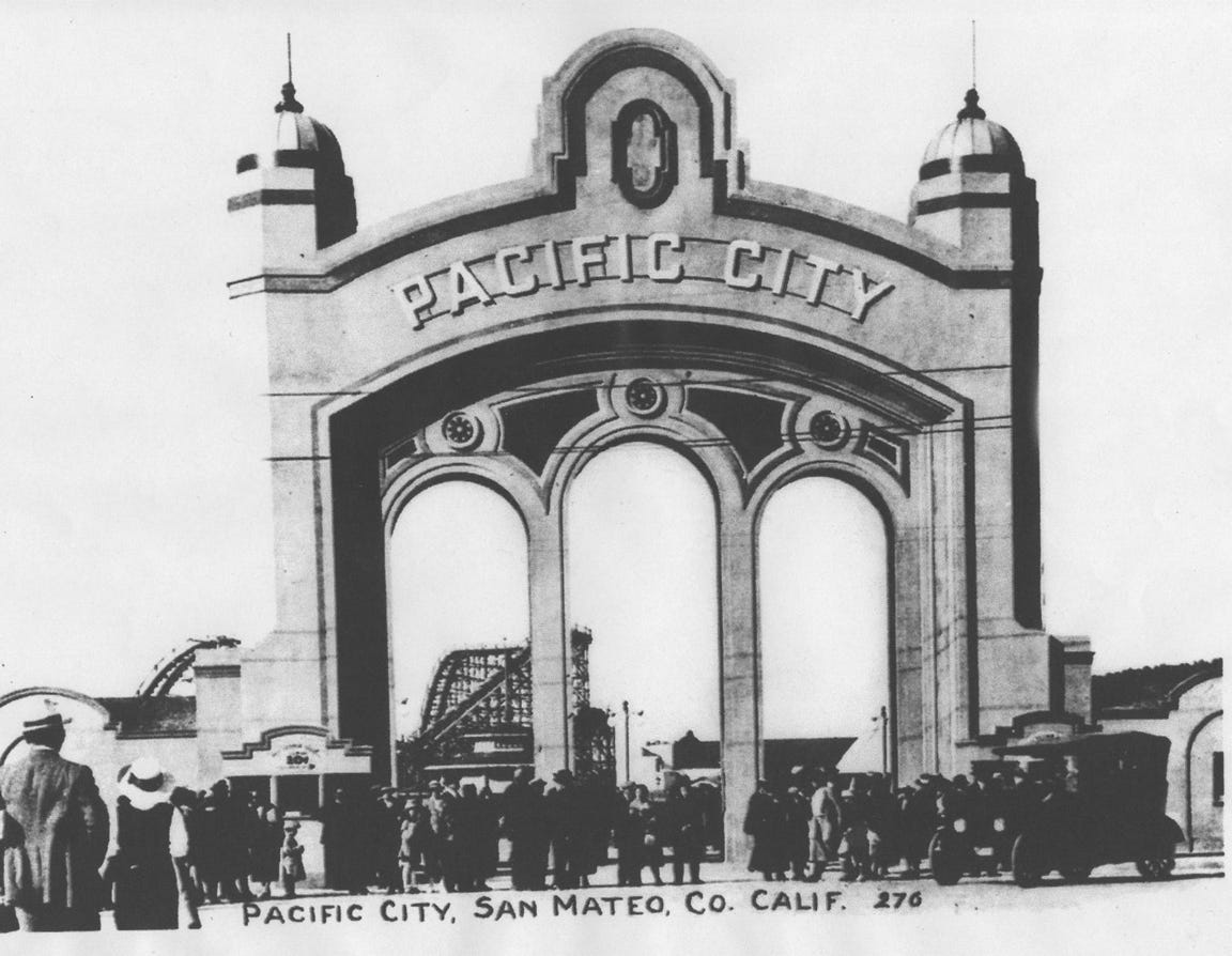old black and white photo showing a small crowd gathered under a tall arch with a sign on it saying Pacific City