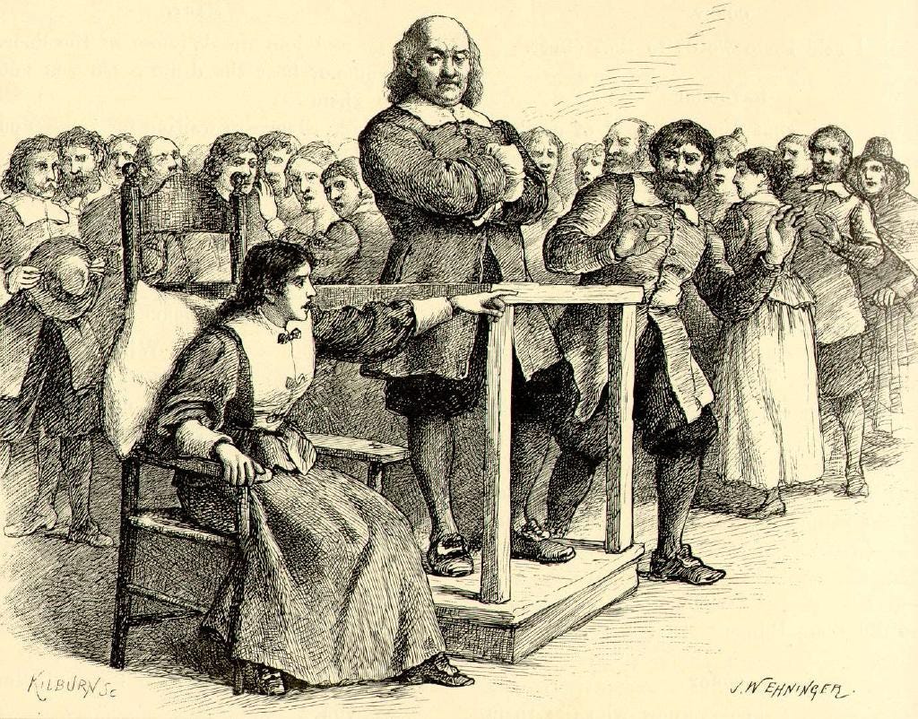 Salem witch trials: A man stand defiantly on trial as a woman sitting next to him points into the stunned crowd