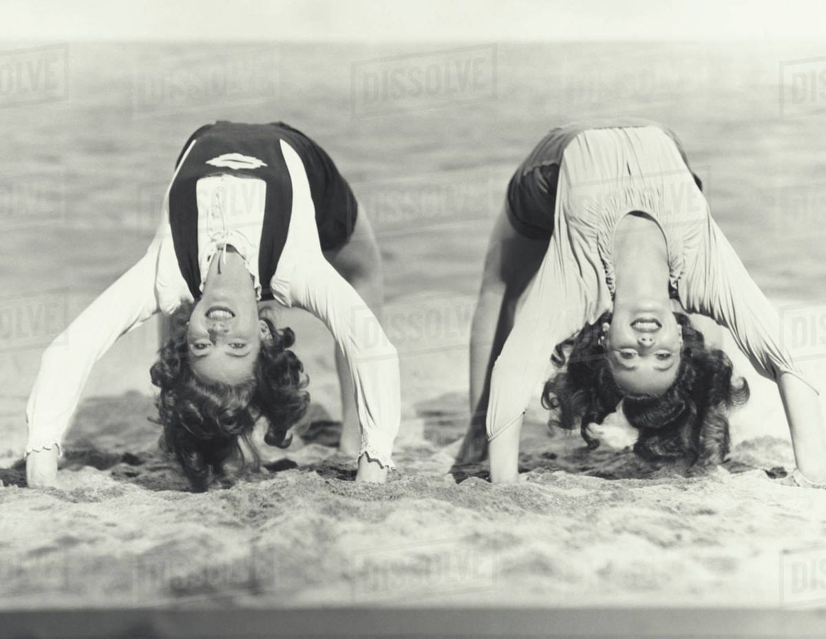 Two women doing backbends on the beach - Stock Photo - Dissolve