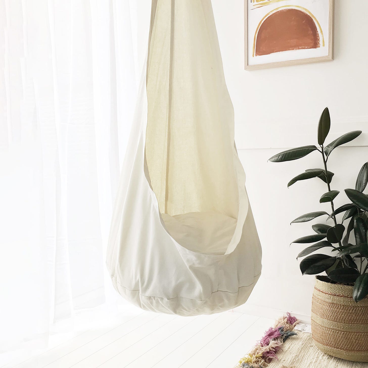 A photo of a sensory swing hanging in a room with a plant beside it 