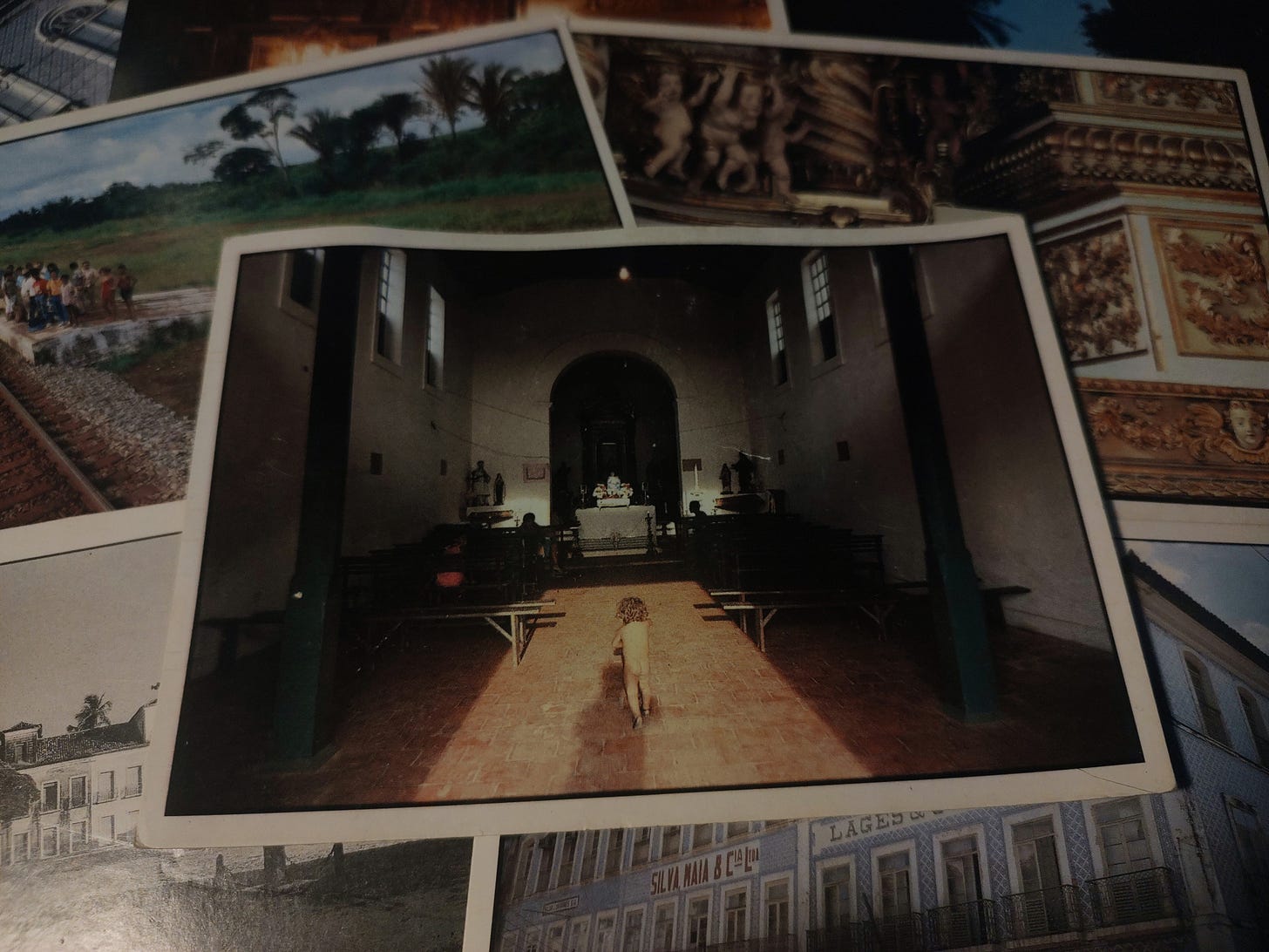 cartão postal com foto do interior de uma igreja católica. a luz do sol entra pela porta principal e uma criança anda pelada em direção ao altar.