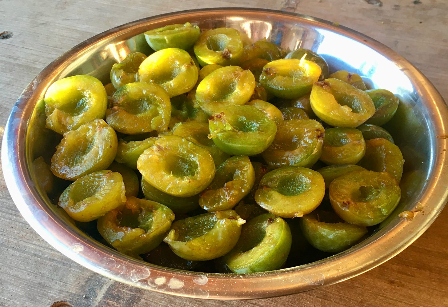 Halved and pitted green plums in a stainless steel bowl