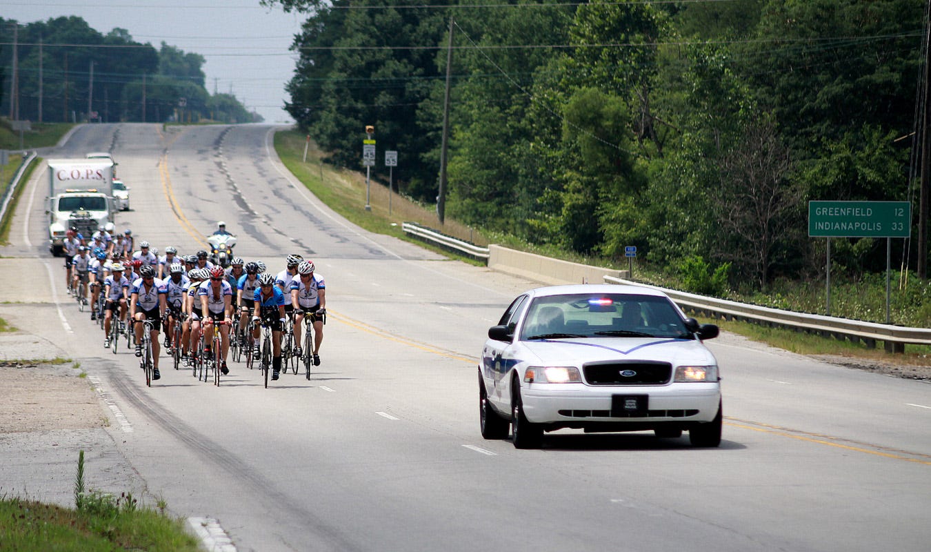 Concerns of Police Survivors (COPS) is an organization that assists the families of Indiana law enforcement officers killed in the line of duty. To bolster its funding, the group sponsors an annual cycling event which takes participants (most police officers) around the state on a fundraising tour. In 2011, the COPS crew came to Knightstown, stopping at a local residence for lunch and rest. In this photo, the COPS bunch pedals into town from the west, along U.S. 40.