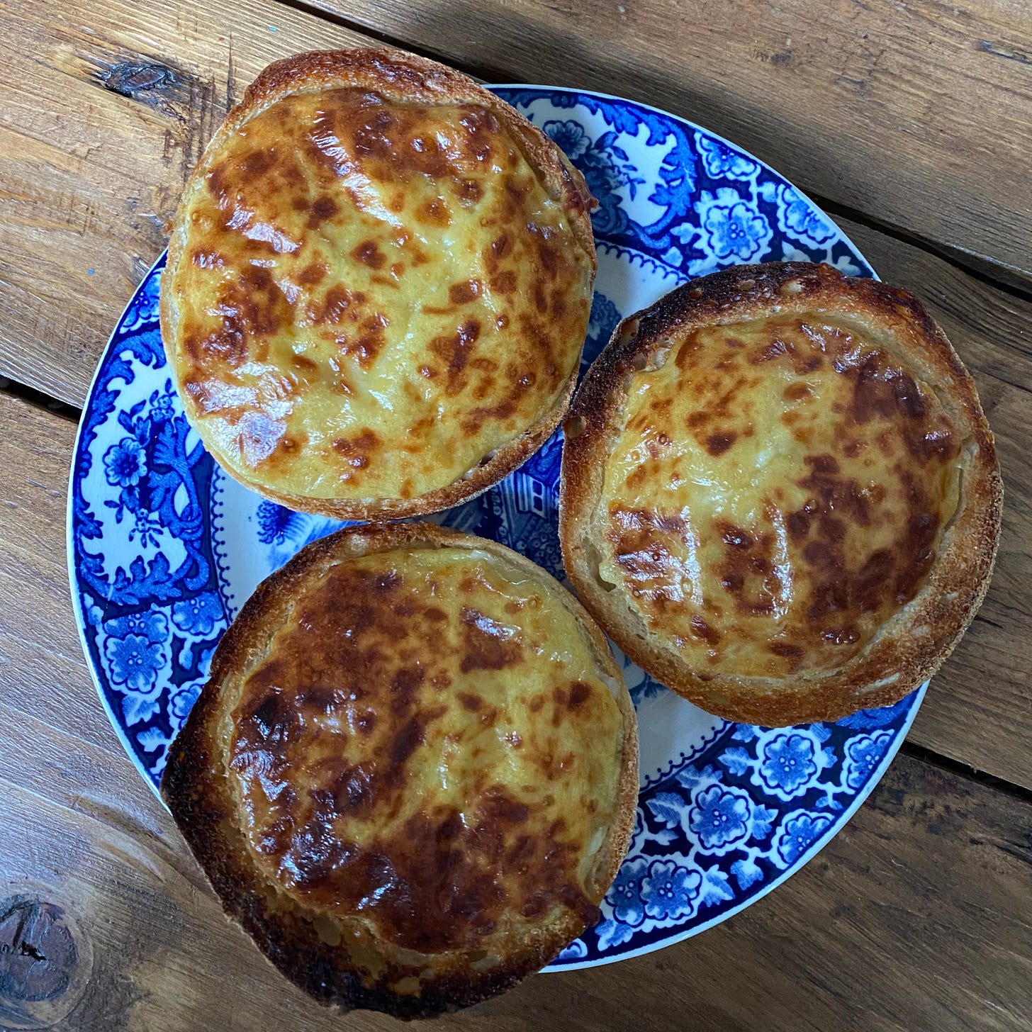 Three english muffins topped with Welsh Rarebit, on a blue & white plate